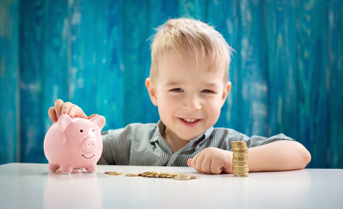 three years old child sitting st the table with money and a piggybank. Happy boy with euro coins